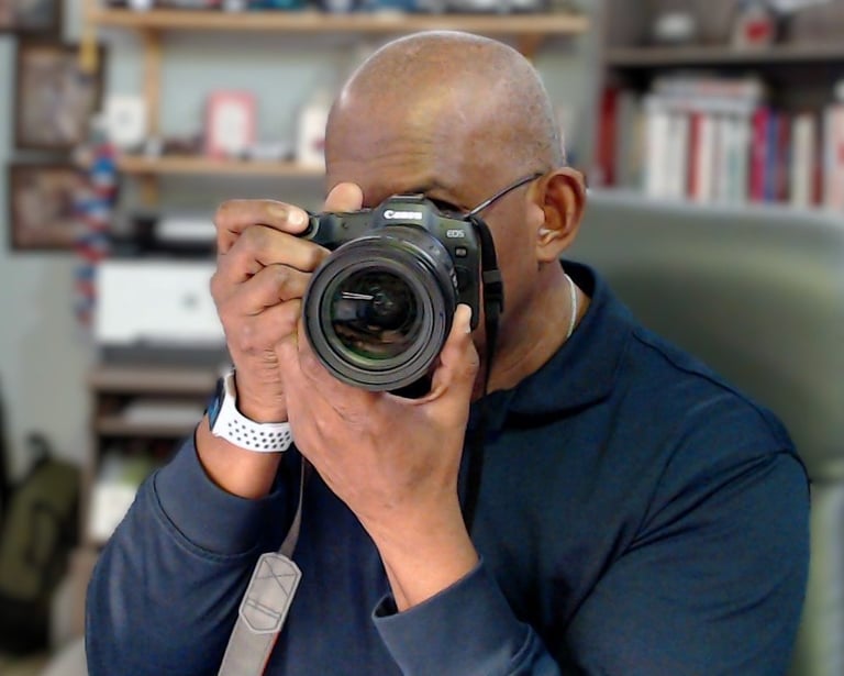 A male photographer holding a professional Canon EOS DSLR camera to his eye to take a picture.