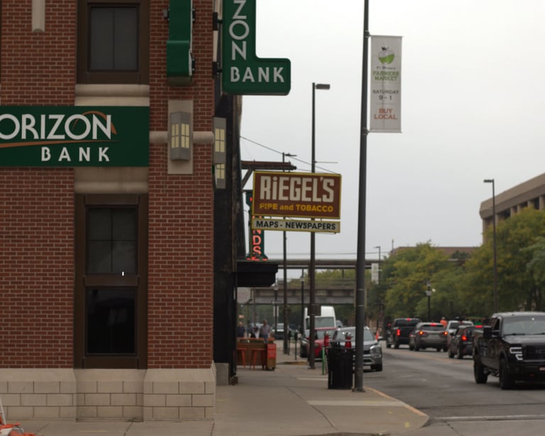 Exterior of Horizon Bank and Riegel's Pipe and Tobacco shop on a busy city street with traffic.