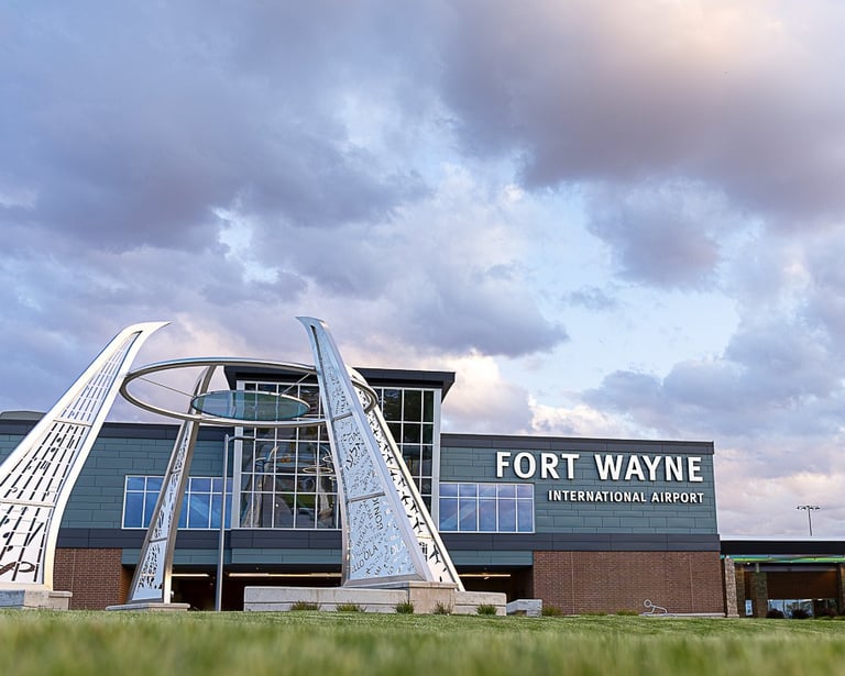 Fort Wayne International Airport terminal building exterior featuring a modern metal sculpture under a cloudy sky.