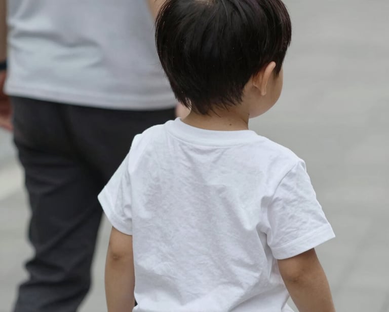 A person sits on a green yoga mat, wearing bright pink leggings and white socks. They hold two small jars, one with a green label reading 'CBD Balm' and the other lid removed, showing its contents. The person wears rings and has black-painted nails.