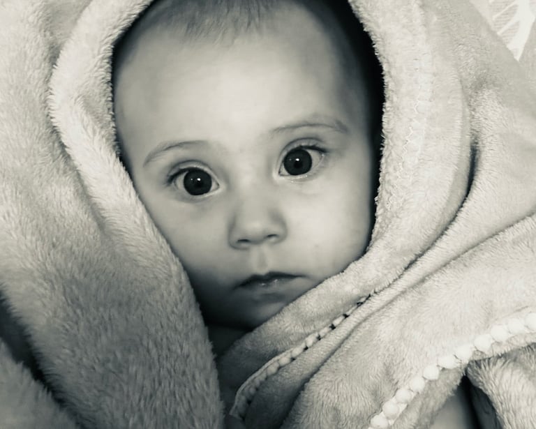 Black and white photo of a baby girl wrapped in a soft blanket, gazing at the camera with wide eyes.