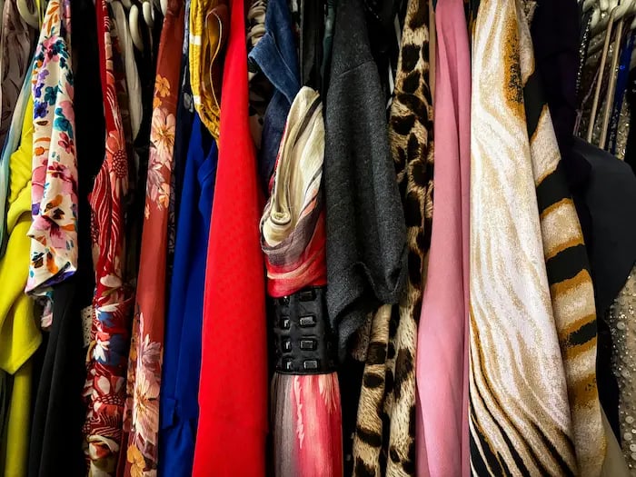 A variety of colorful patterned clothing and dresses hanging on a rack in a closet.