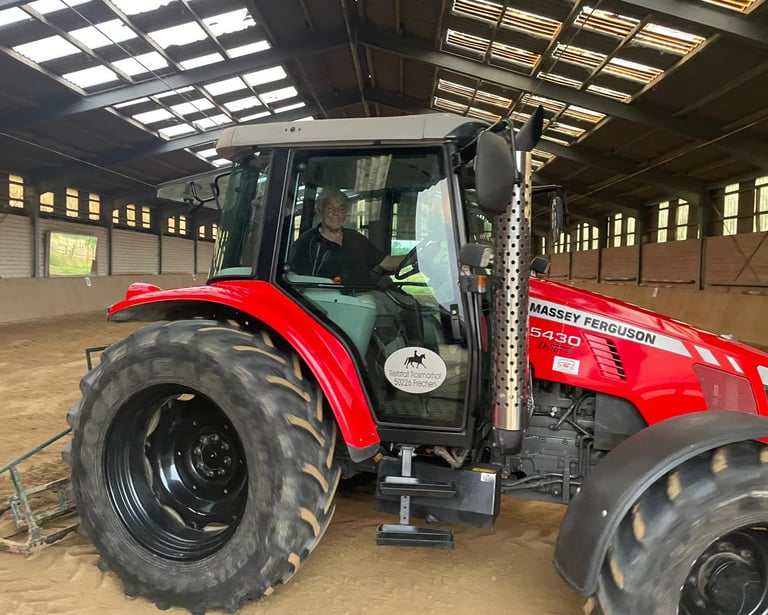 Red Massey Ferguson 5430 tractor leveling the sand in an indoor horse riding arena.