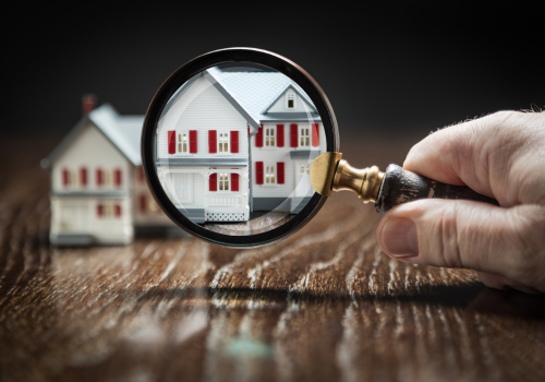 Hand holding a magnifying glass over a model house for real estate inspection and property search.