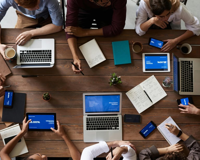 Overhead view of a business team collaborating at a wooden table with laptops and digital tablets.