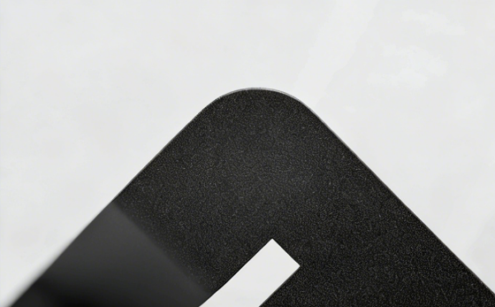 Close-up of a matte black textured metal surface with a rounded corner and a white cutout detail.