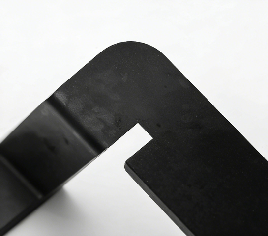 Close-up of a matte black metal furniture leg bracket with a rounded corner and industrial finish.