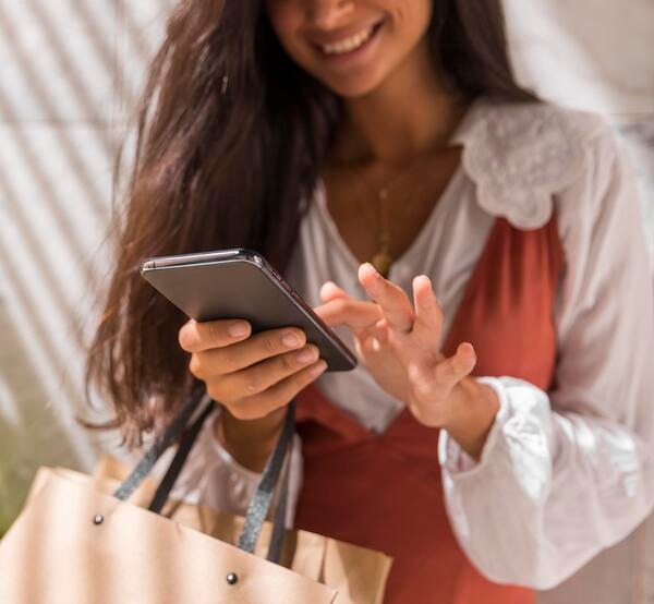 Mujer sonriente sosteniendo bolsas de compras mientras hace compras en línea desde el celular.