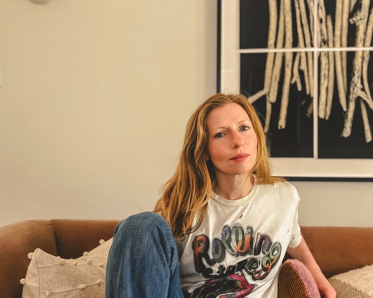 Editorial portrait of a yoga teacher with red hair and somatic practitioner, seated on a sofa. 
