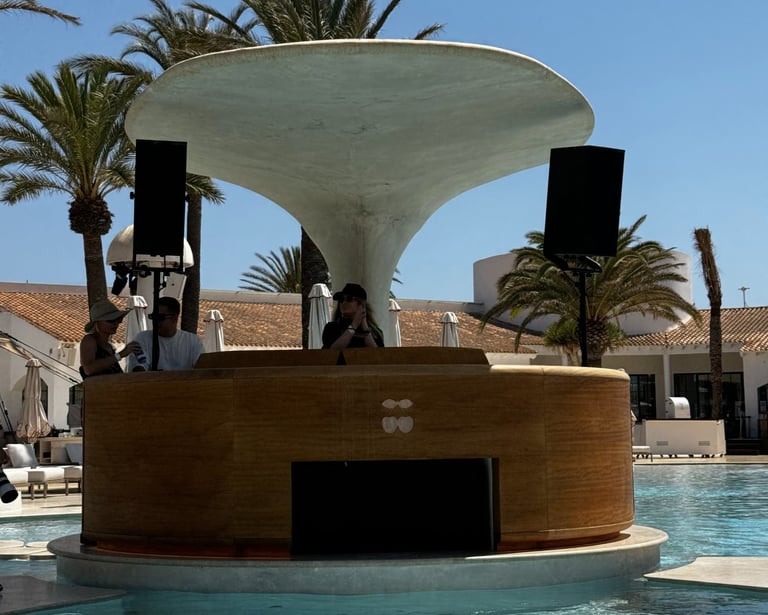 Dj booth - Kat Bendis performing at Destino Ibiza luxury resort swimming pool with palm trees.