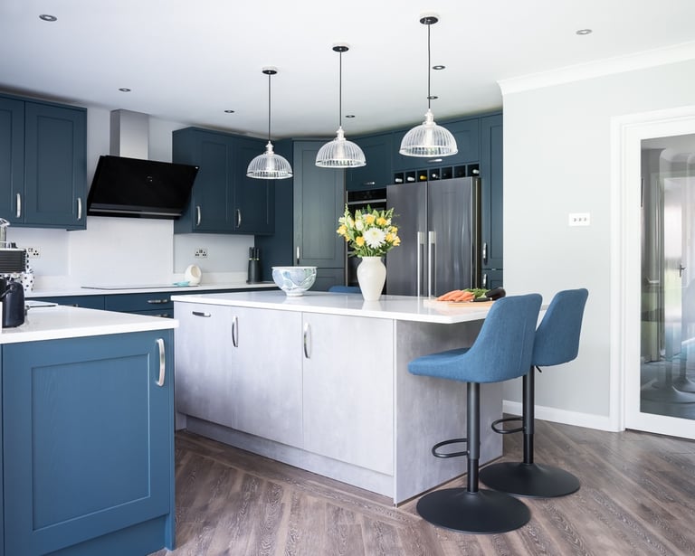 Modern kitchen featuring blue shaker cabinets, a light grey island with seating, and pendant lighting.