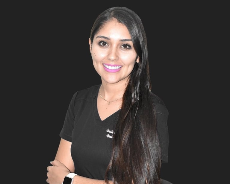 Smiling female medical professional with long dark hair wearing black scrubs against a dark background.