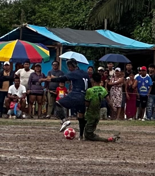 Local soccer players competing on a muddy field during a match in front of a crowd.