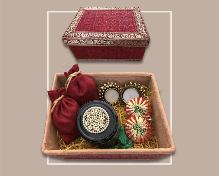 Traditional red textured festive gifting hamper with gold embroidery and diyas.