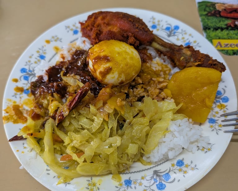 A plate of Nasi Kandar with fried chicken, boiled egg, cabbage, and curry gravy.