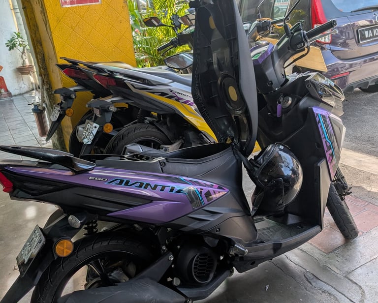 A purple Yamaha Ego Avantiz scooter with its seat open parked on a street in Malaysia.