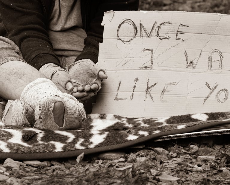 Morador de rua sentado com um cartaz, simbolizando desigualdade e exclusão social.
