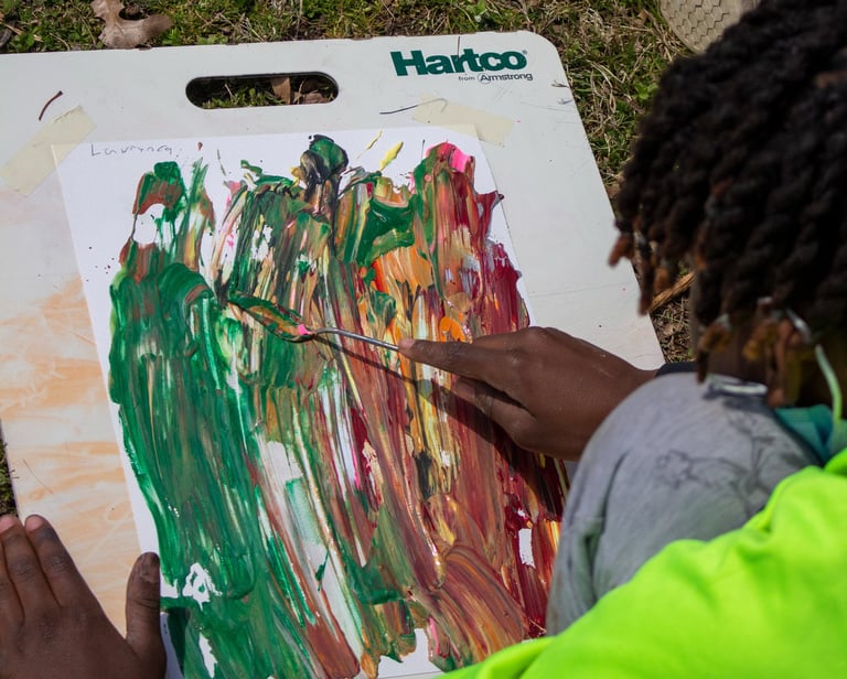Young boy using a palette knife to smooth paint dabs over a paper.