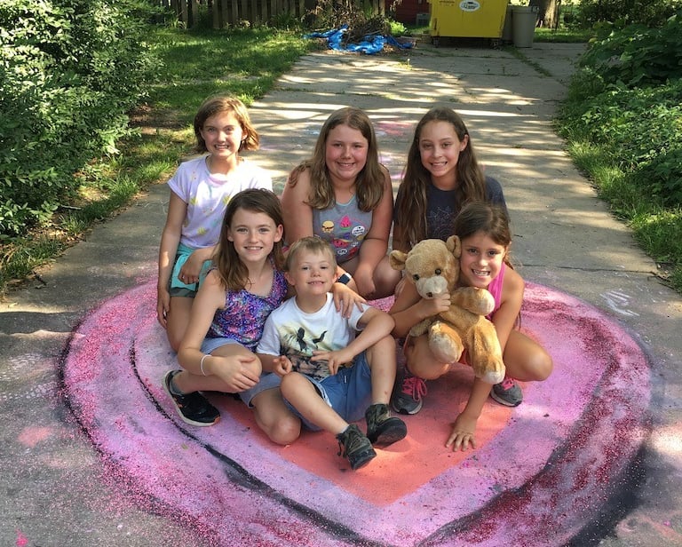 Group of smiling children posing on top of a large chalk heart they made.