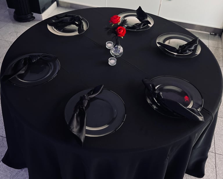 Elegant round table with a black tablecloth, charger plates, black satin napkins, and a centerpiece.