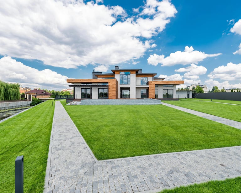 Modern luxury house with wood paneling, a large green lawn, and stone walkways under a blue sky.