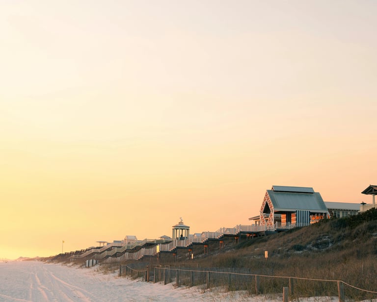 Luxury beachfront pavilions and coastal architecture along a white sand beach at sunset.