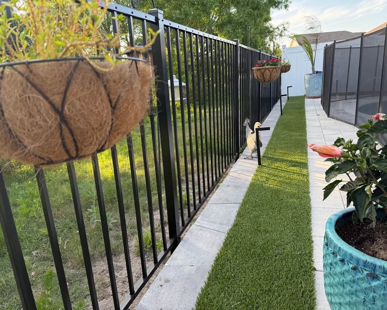 Black metal pool fence with hanging flower baskets and artificial grass turf walkway.