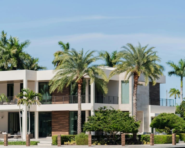 Modern luxury waterfront mansion with palm trees and a private dock on a sunny day.