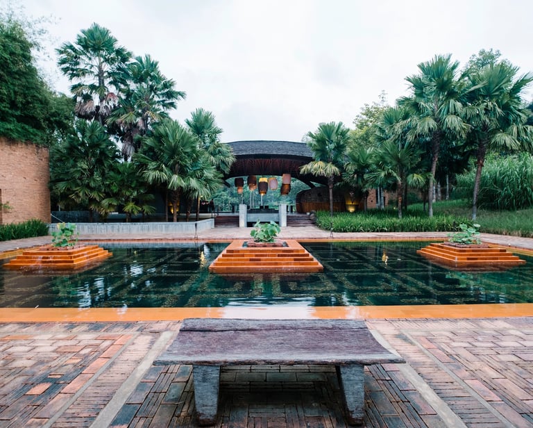 Luxury tropical resort courtyard featuring a tiered reflection pool, palm trees, and stone architecture.