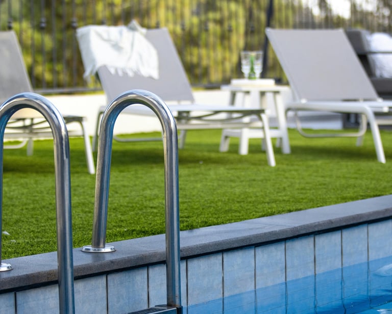 Stainless steel swimming pool ladder handrail on a luxury patio with artificial grass and lounge chairs.