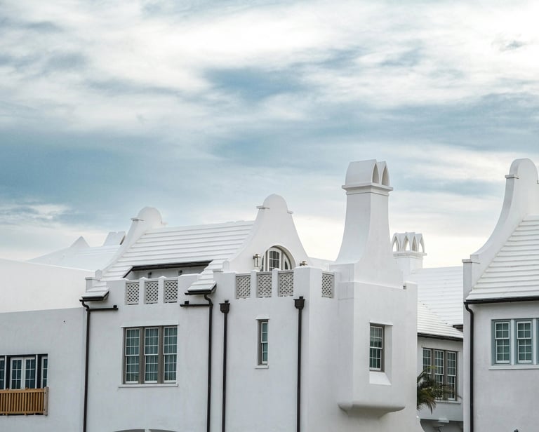 White stucco coastal architecture with iconic stepped chimneys and tile roofs under a cloudy sky.