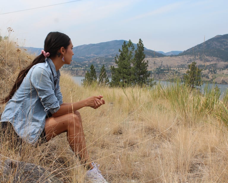 a person sitting on a hill looking at a lake in the distance