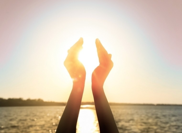 Deux mains levées encadrant le soleil au bord de l’eau
