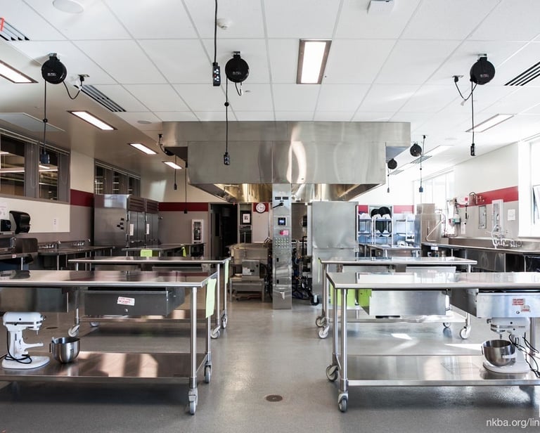 Wide shot of a professional kitchen with stainless steel workstations. Discover more about us.