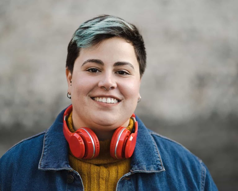 Smiling person with short blue-tipped hair wearing red headphones and a denim jacket.