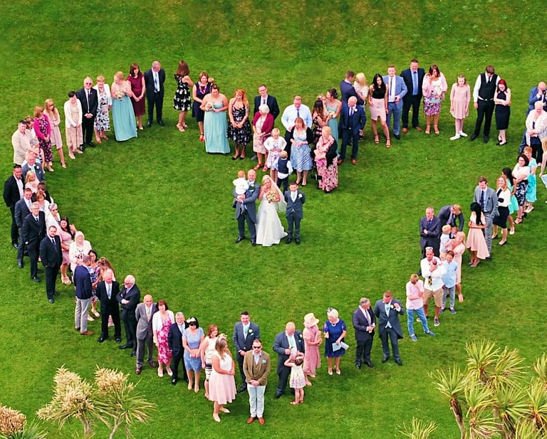 Aerial photo of people at a wedding positioned to form a heart around the bride and groom