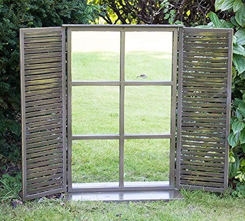 Rustic garden mirror with shutters reflecting a green lawn to create a window effect in a backyard.