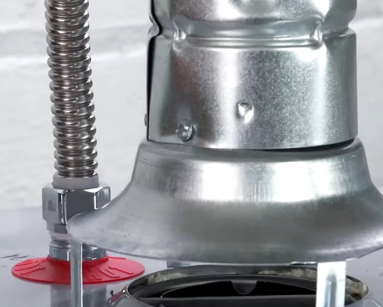 Close-up of a gas water heater draft hood and flexible stainless steel water connector.