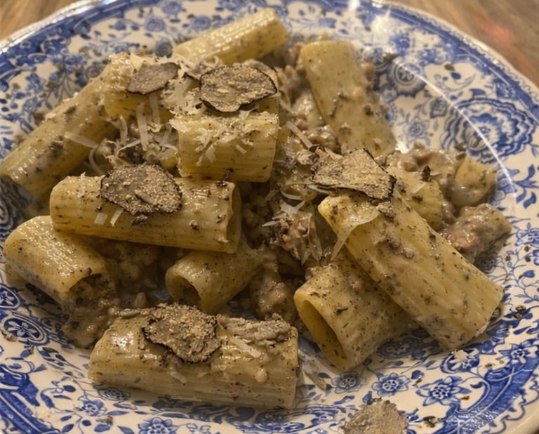 Rigatoni pasta with creamy truffle sauce and fresh black truffle shavings on a blue floral plate.