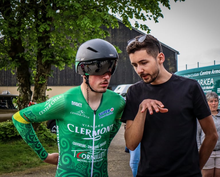 Professional cyclist in green team jersey and aero helmet discussing race strategy with his coach.