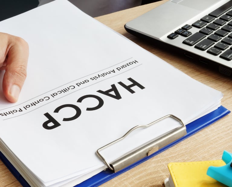 A person reviews a HACCP hazard analysis and critical control points document on a blue clipboard.