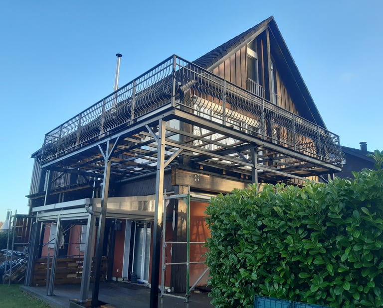 Modern house with a large elevated steel balcony structure and metal railing under a clear blue sky.