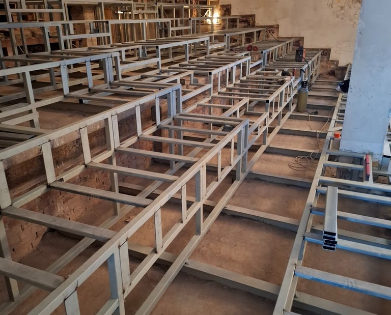 Steel tier seating frame under construction inside a renovated auditorium or lecture hall.