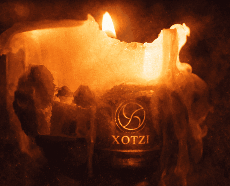 Una vela naranja brillante, con cera derritiéndose y una llama encendida, que presenta un logo xotzi