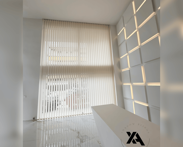 Modern office reception area with white vertical blinds covering large windows and a contemporary white reception desk.