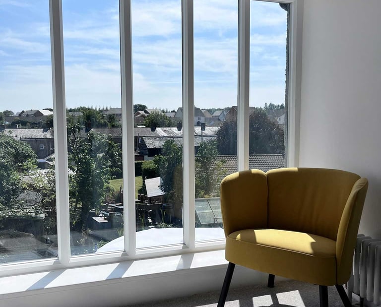 Mustard coloured chair next to large sunny window with village views