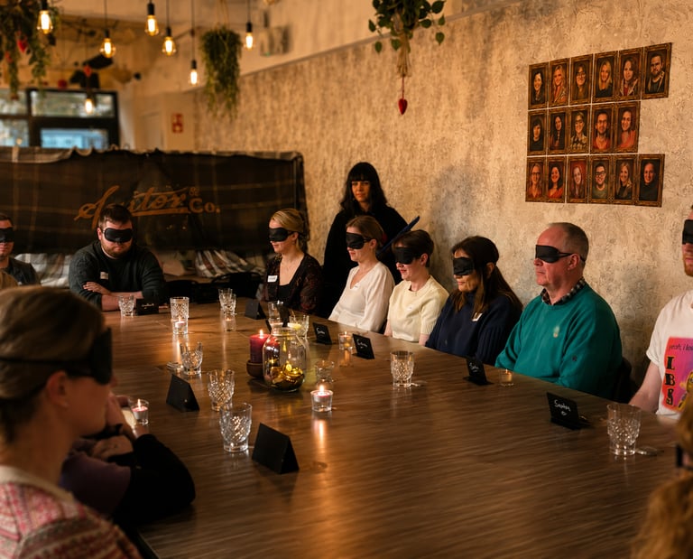 People are sitting at a table playing a Traitors game. They are blindfolded.