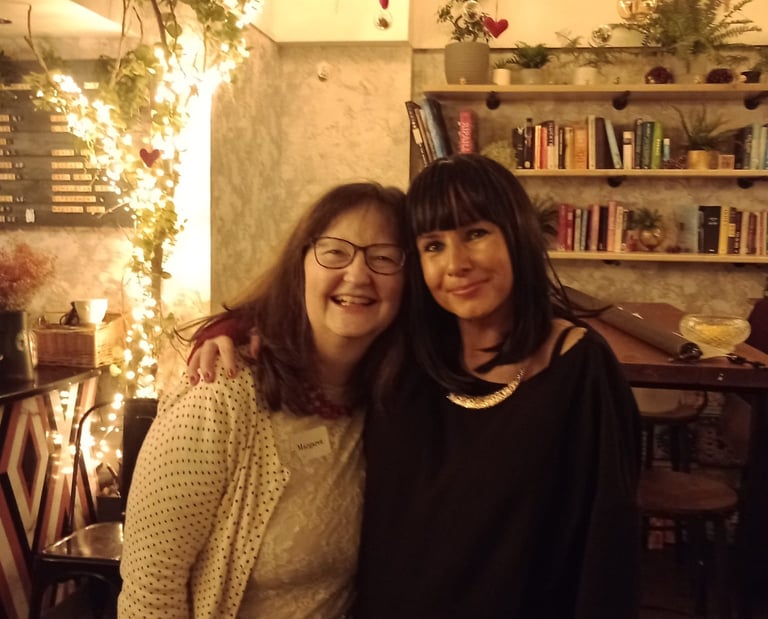 two woman have their arms around each other. They are smiling. They are at a Traitors themed party.