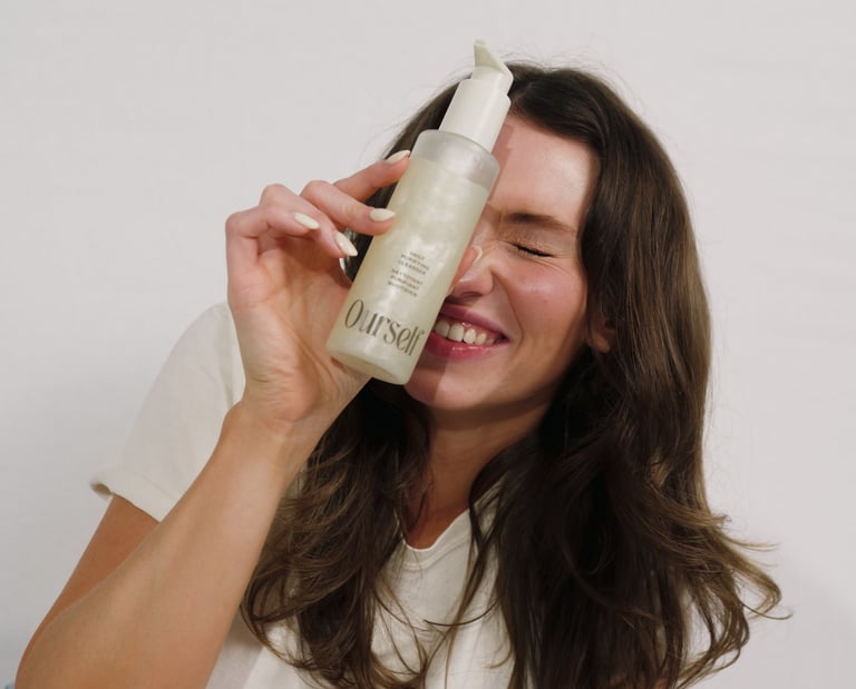 A smiling woman holding a bottle of Ourself daily purifying facial cleanser against her face.