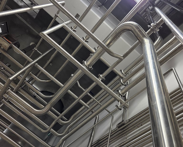 Wide view of industrial stainless steel piping and plumbing fixtures in a modern factory facility.